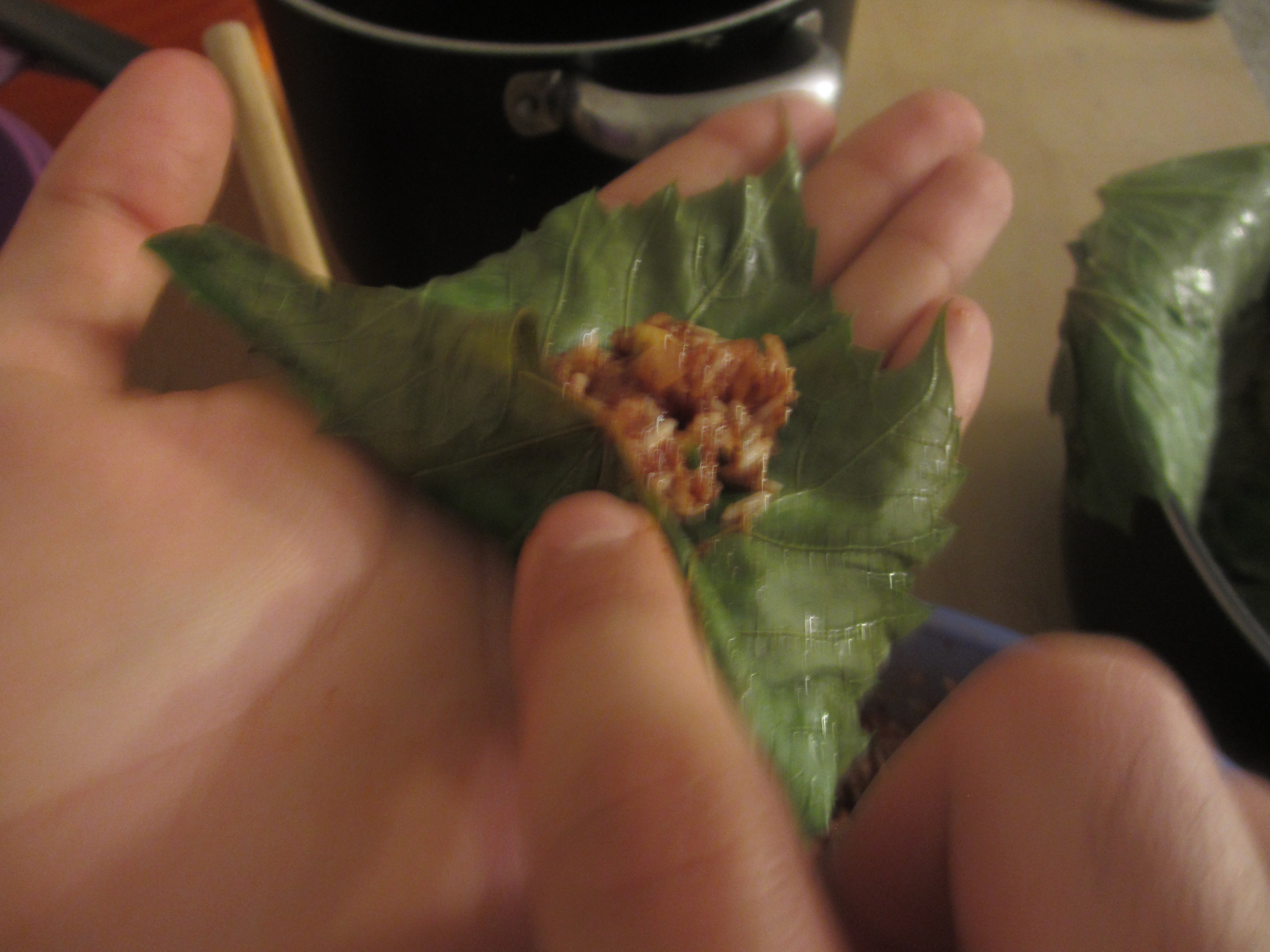 Grape leaf being stuffed on the palm of a hand