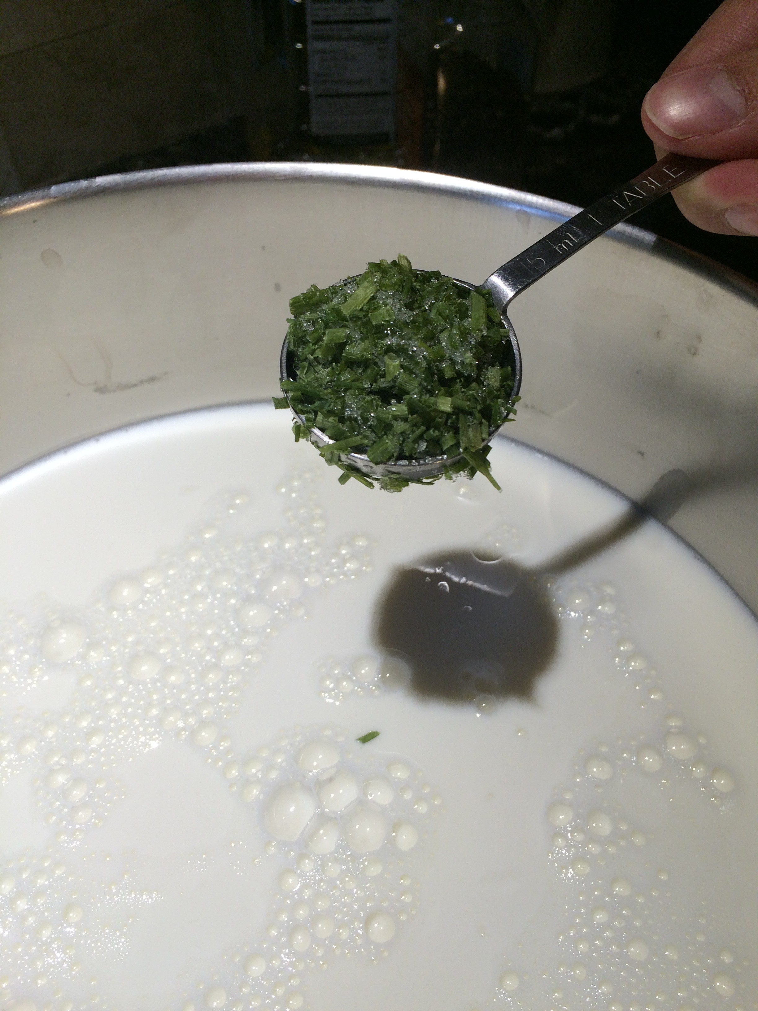 Adding a spoon of chopped chives to a pot of milk