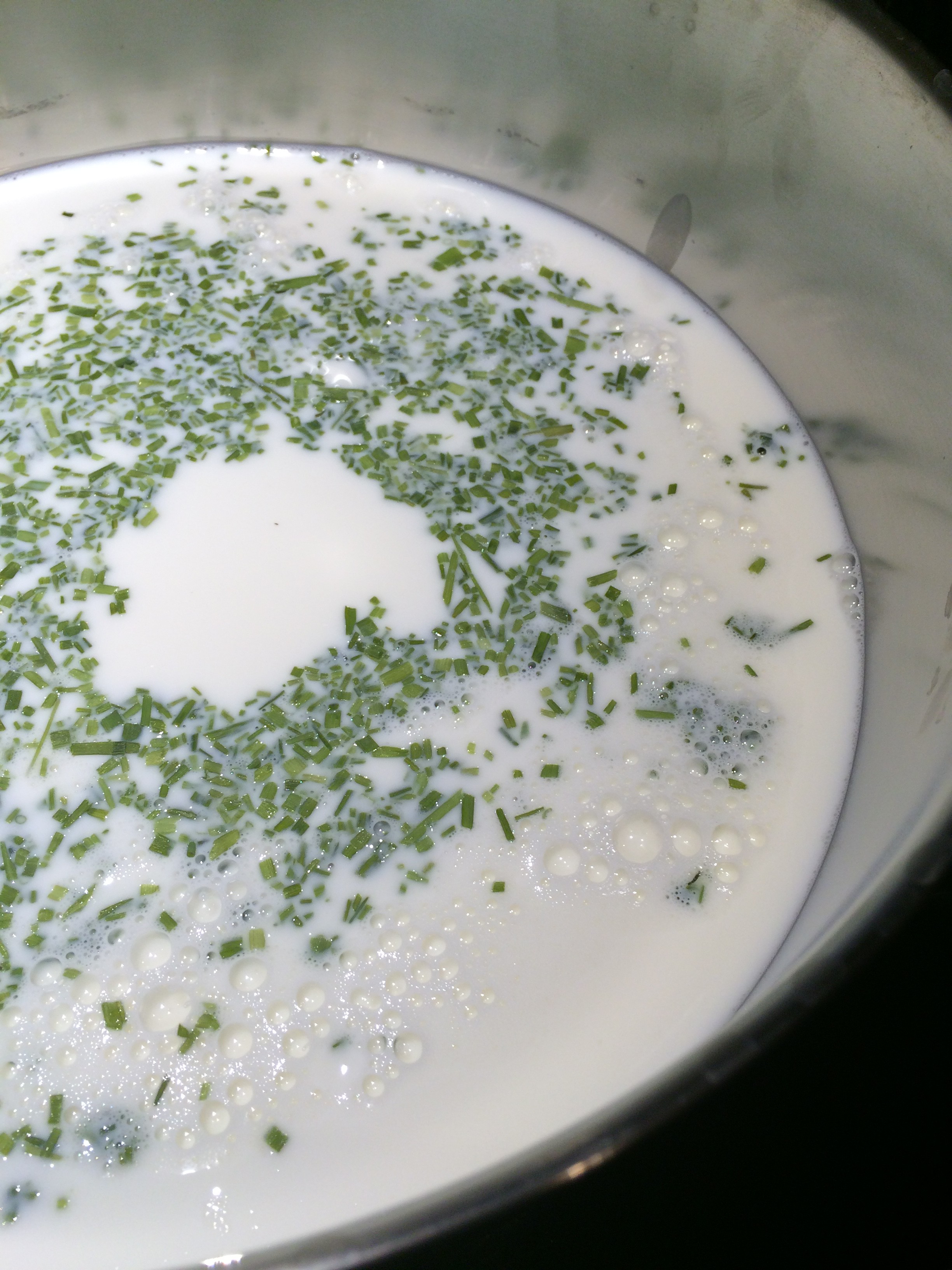Milk in a pot, being heated on low heat, with chives