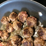 Meatballs, seared and cooking in a sauce pan.