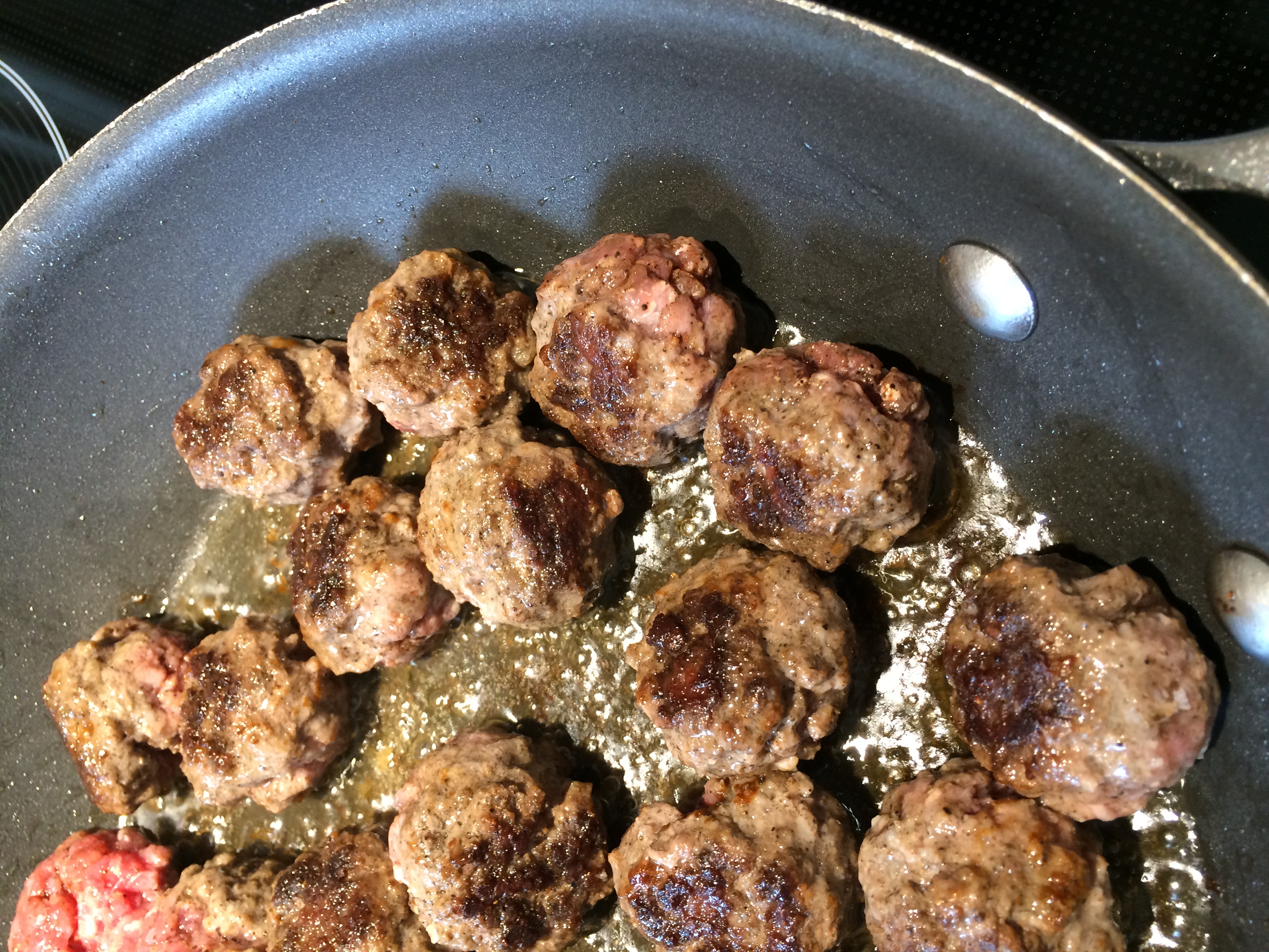 Meatballs, seared and cooking in a sauce pan.