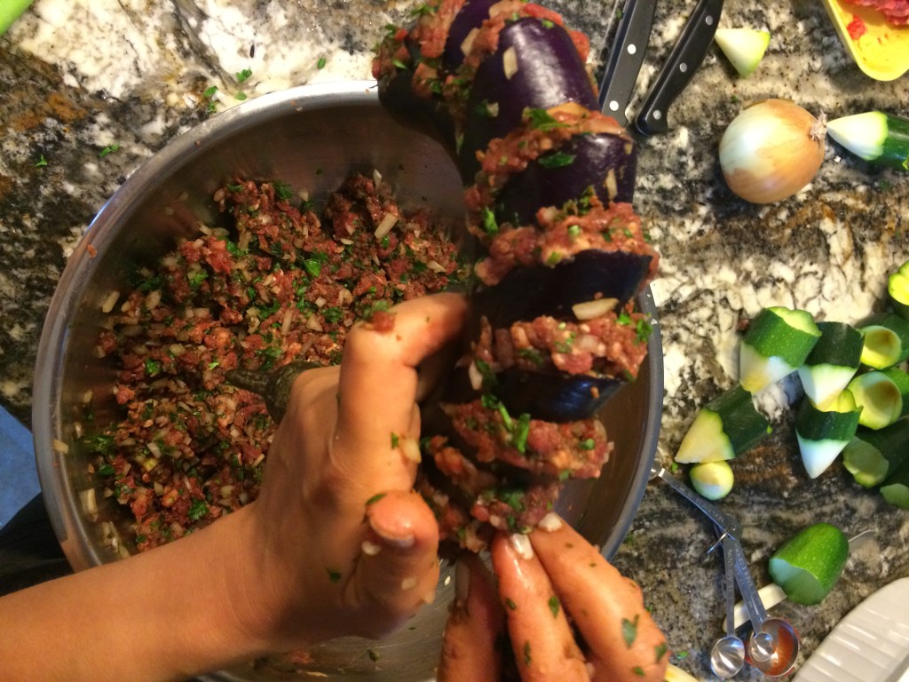 Hands stuffing meat into a sliced chinese eggplant